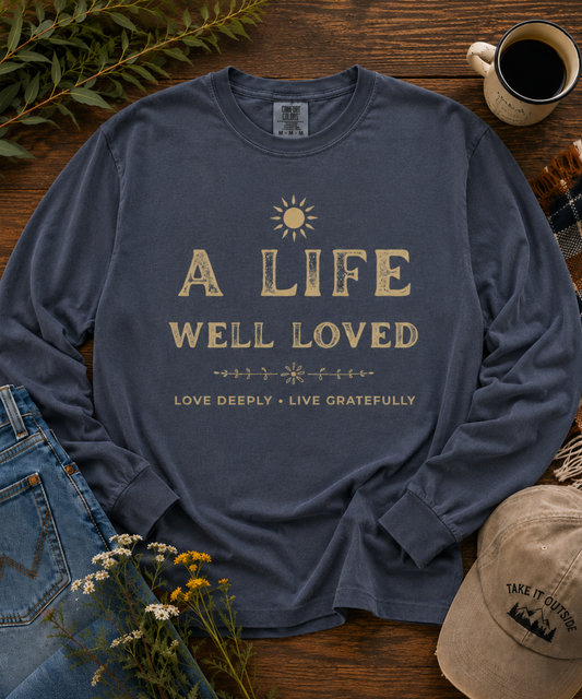 Denim blue A Life Well Loved vintage inspirational long sleeve T-shirt styled in a rustic outdoor-inspired flat lay.