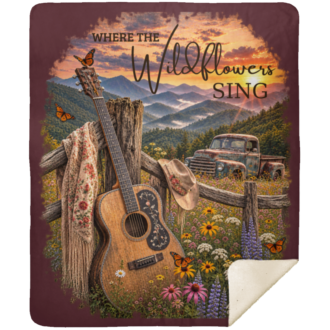 A sherpa fleece blanket with a rustic country design, featuring an acoustic guitar, a cowboy hat, mountains, a pickup truck, and the text 'WHERE THE Wildflowers SING'. The blanket has a maroon border and a cream-colored reverse side with a curled corner, shown against a plain white background.