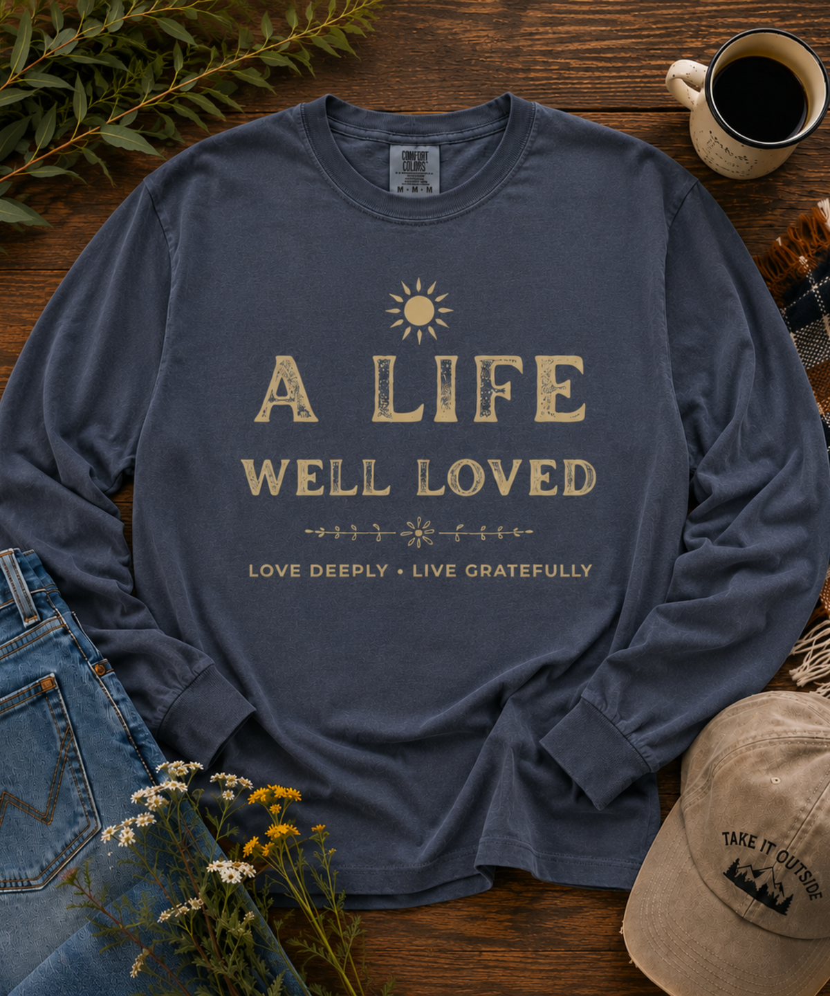 Denim blue A Life Well Loved vintage inspirational long sleeve T-shirt styled in a rustic outdoor-inspired flat lay.