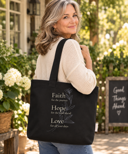 Woman carrying black Christian tote with Faith Hope Love botanical design in a warm garden setting.