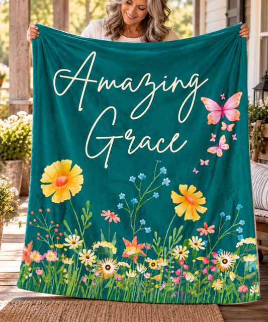 Mature woman holding an Amazing Grace dark teal blanket with colorful wildflowers and butterflies on a sunny porch.
