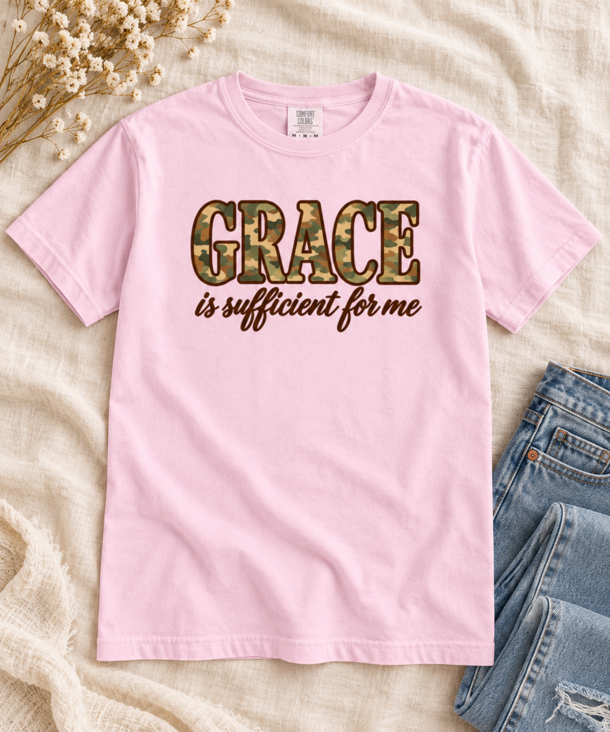 A light pink short-sleeve t-shirt with the text 'GRACE is sufficient for me' printed on the front. The word 'GRACE' is filled with a camouflage pattern, while 'is sufficient for me' is in brown cursive.