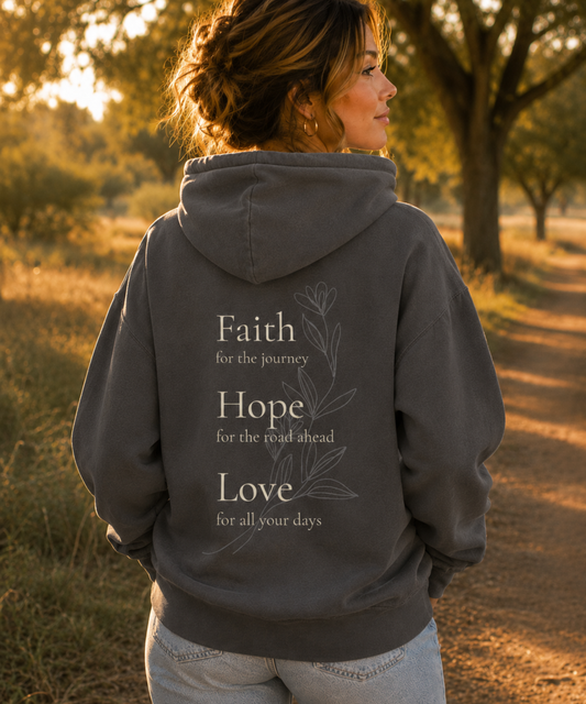 Back view of woman wearing Comfort Colors pepper hoodie with Faith Hope Love botanical Christian back design outdoors