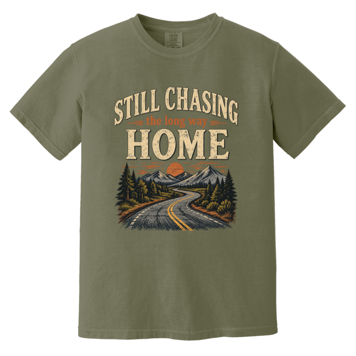 A moss green short-sleeve t-shirt with a vintage-style graphic on the front that reads 'STILL CHASING the long way HOME' above an illustration of a winding road through pine trees and mountains.