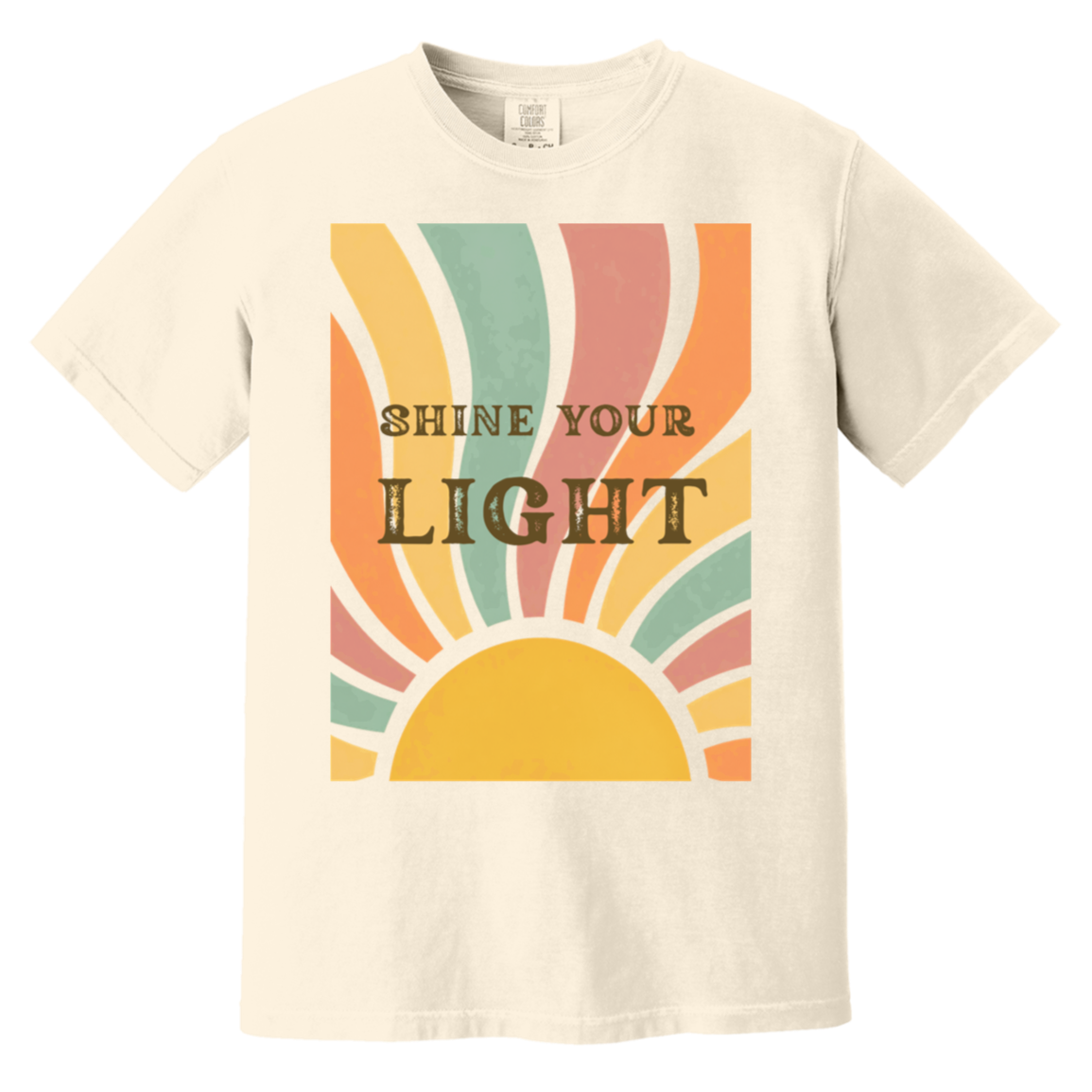 An ivory comfort colors crewneck t-shirt featuring a retro-style graphic of a rising sun with the text 'SHINE YOUR LIGHT' in dark brown lettering, set against a plain white background.