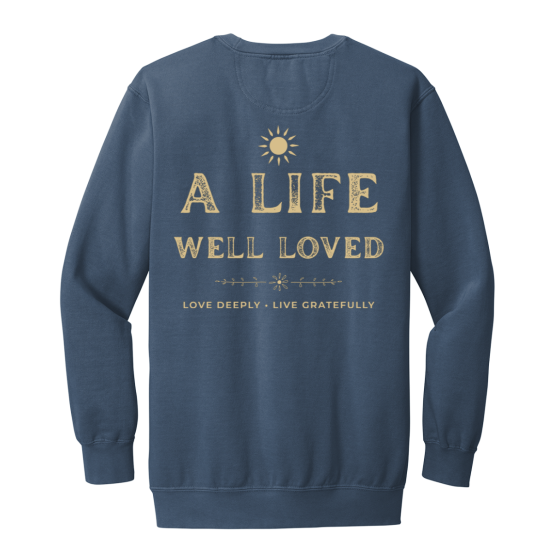 A blue jean crewneck sweatshirt with a distressed gold graphic on the back that reads 'A LIFE WELL LOVED' and 'LOVE DEEPLY • LIVE GRATEFULLY' with a small sun icon above, shown on a plain white background.