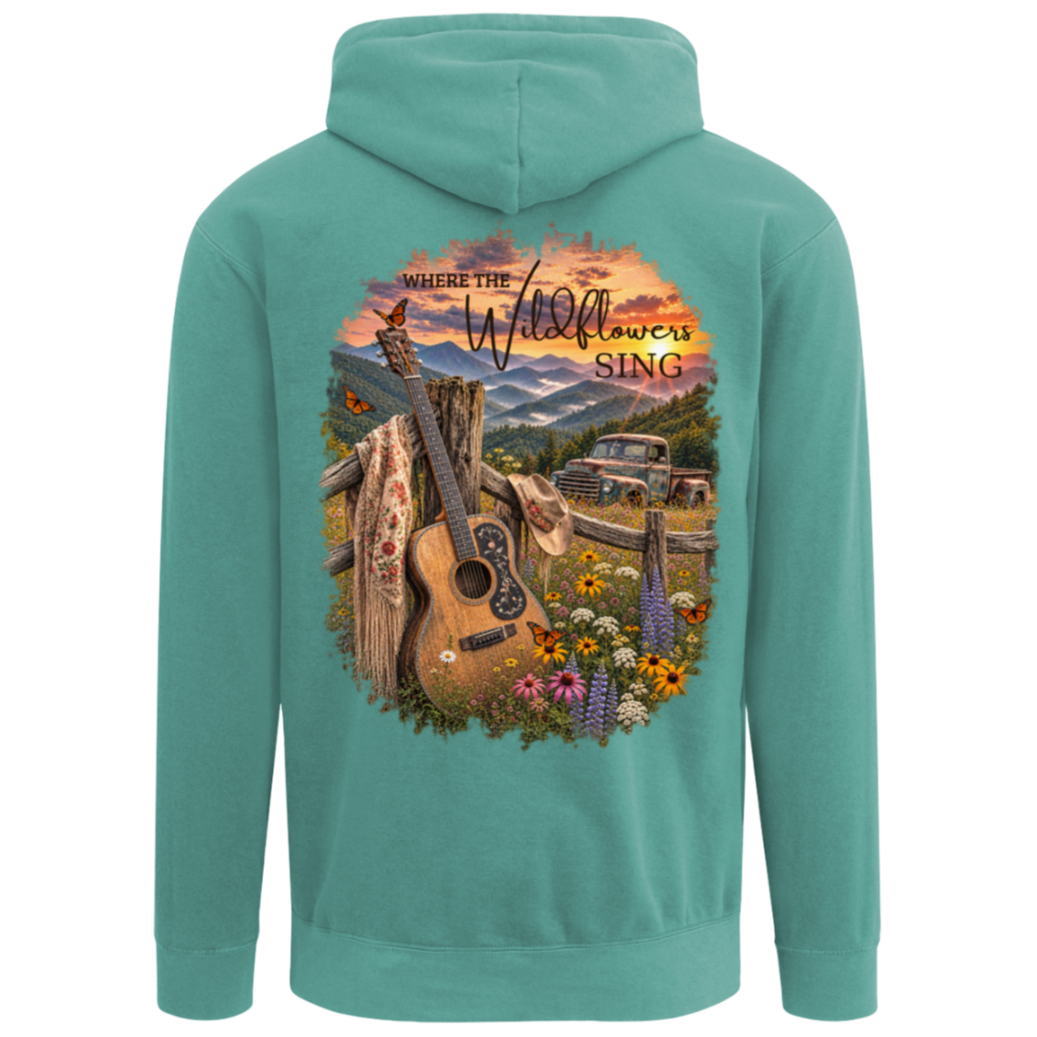A seafoam green hoodie shown from the back, featuring a large graphic print of an acoustic guitar, wildflowers, a rustic fence, mountains, and an old pickup truck under a sunset sky with the text 'Where the Wildflowers Sing'.