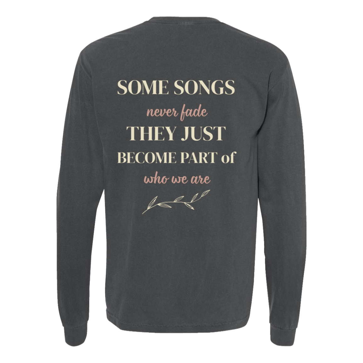 A pepper comfort colors long-sleeve t-shirt shown from the back, featuring a printed quote in cream and dusty pink text that reads 'SOME SONGS never fade THEY JUST BECOME PART of who we are' with a small leafy branch illustration below.