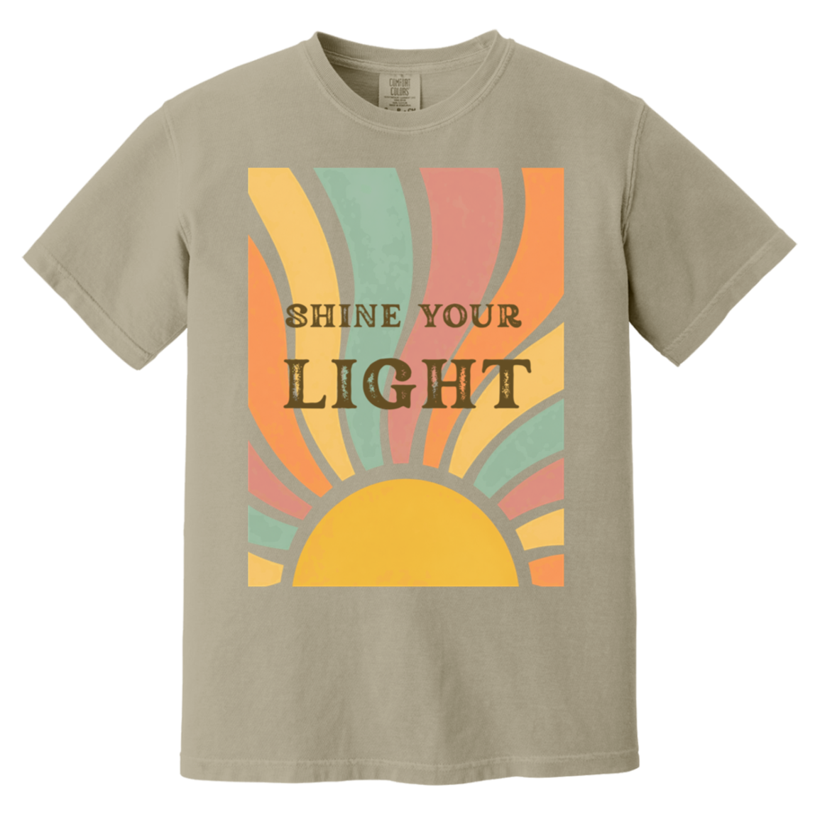 A sandstone comfort colors crewneck t-shirt featuring a retro-style graphic of a rising sun with the text 'SHINE YOUR LIGHT' in dark brown lettering, set against a plain white background.