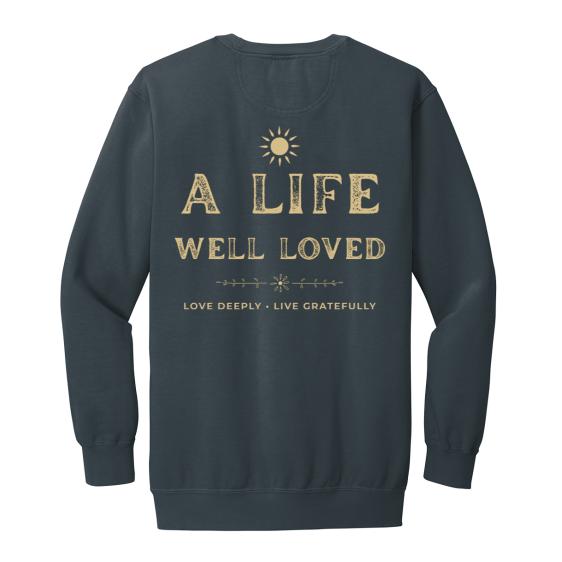 A denim crewneck sweatshirt with a gold graphic print on the back. The print features a sun icon above the distressed text 'A LIFE WELL LOVED' and 'LOVE DEEPLY • LIVE GRATEFULLY'.