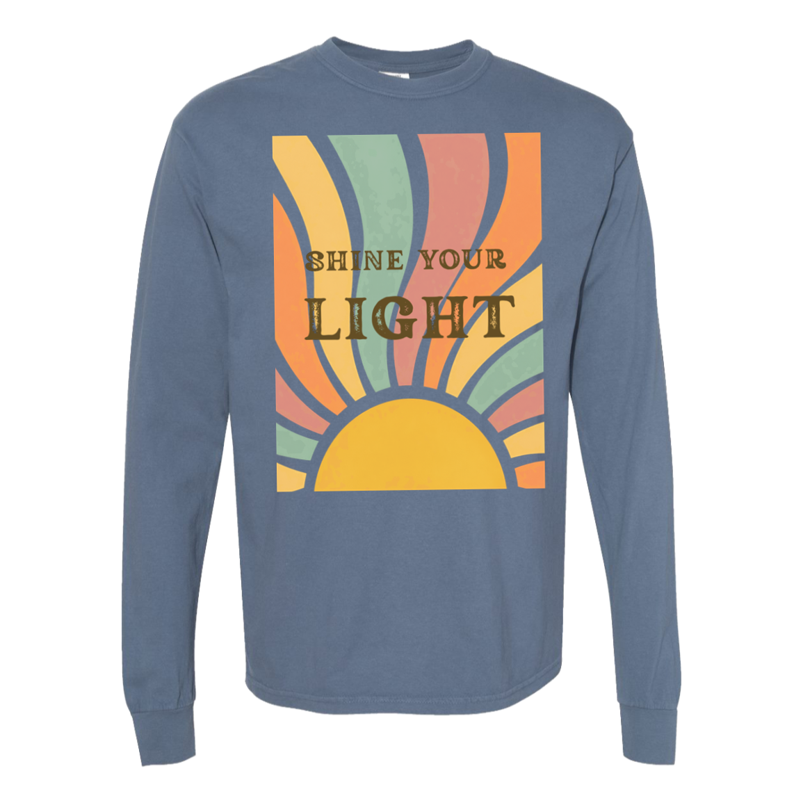 A comort colors long-sleeve crewneck t-shirt in blue jean, featuring a retro-style graphic on the chest with a semi-circle sun and curved rays in yellow, orange, green, and pink, with the text 'SHINE YOUR LIGHT' printed in brown.