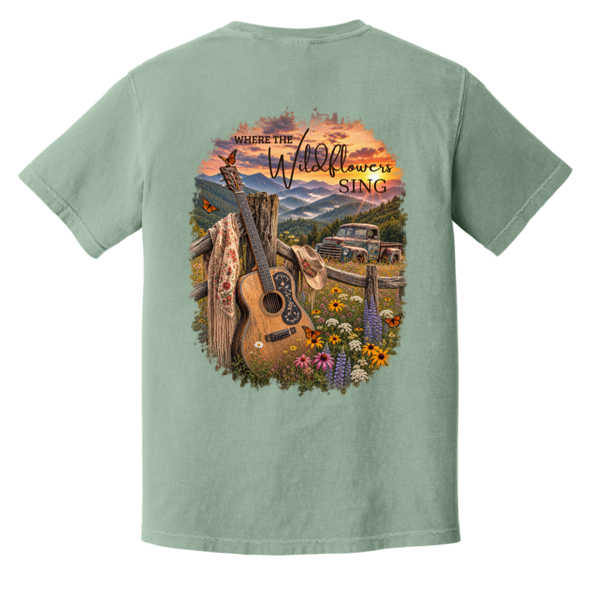 A bay green short-sleeve t-shirt shown from the back, featuring a large, colorful graphic print of an acoustic guitar, a rustic truck, mountains, and wildflowers under a sunset sky with the text 'Where the Wildflowers Sing'.
