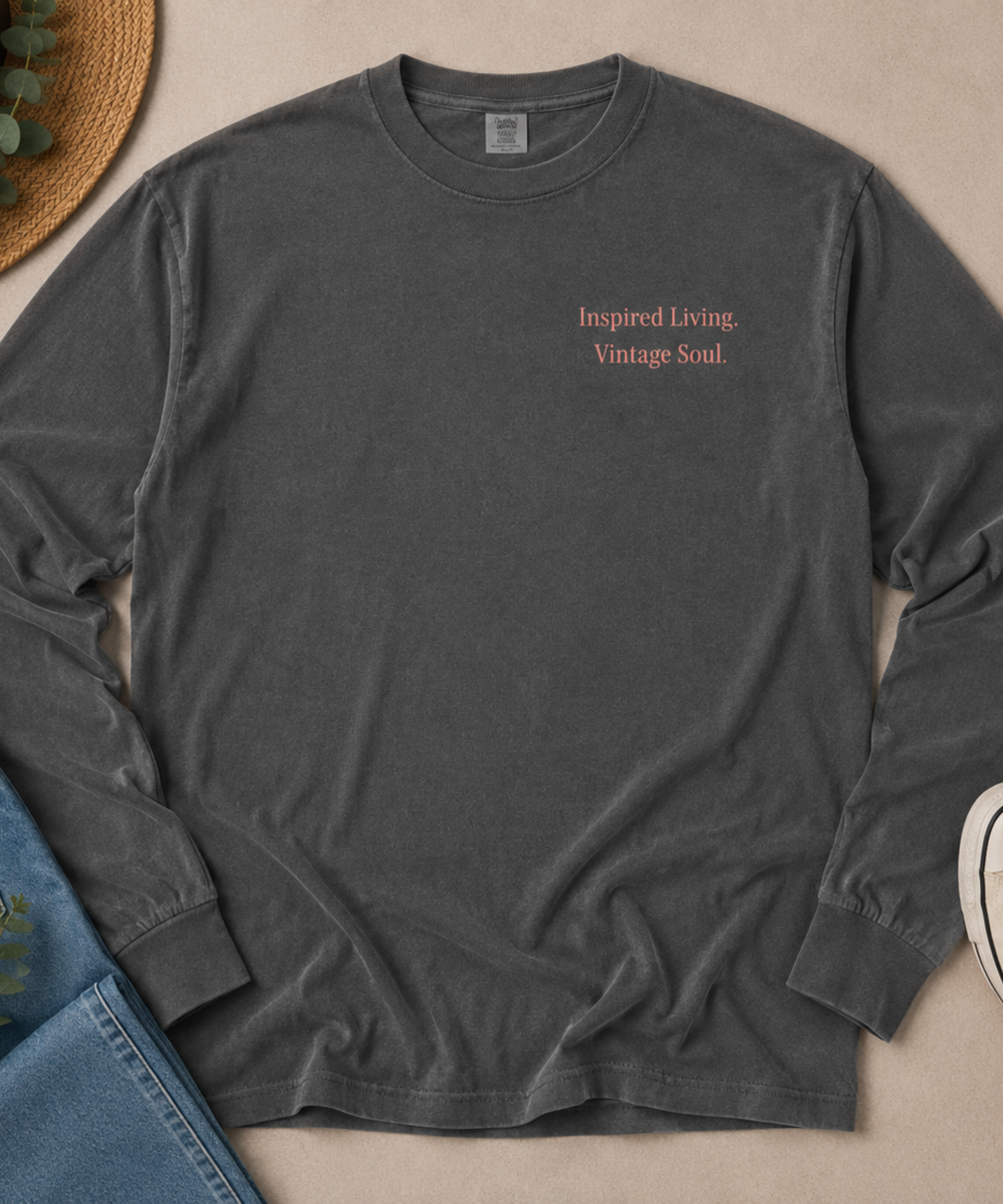 Flat lay of a Comfort Colors Pepper long sleeve T-shirt with the Inspired Living. Vintage Soul. left chest design, styled with blue jeans, canvas sneakers, and a straw hat.