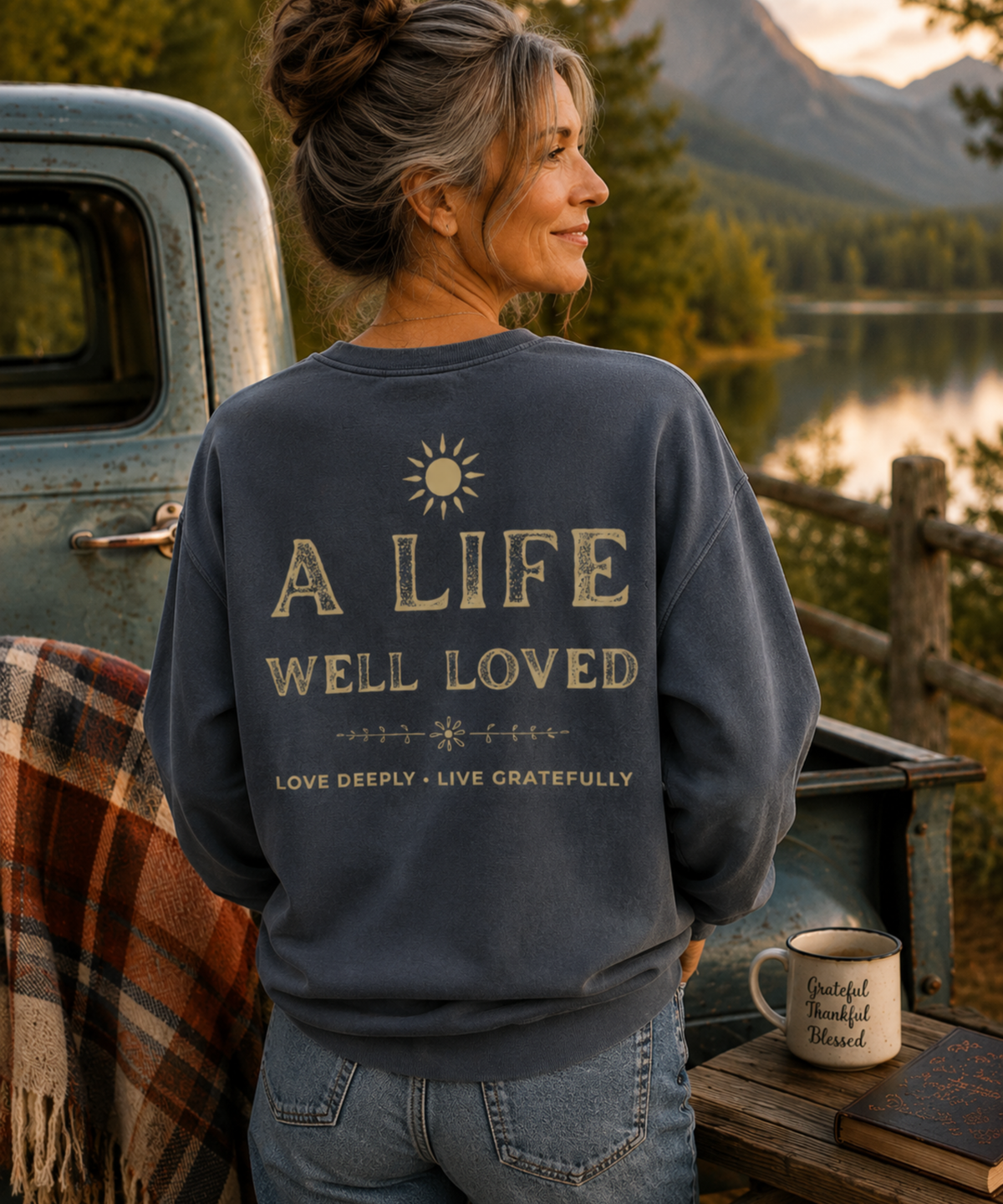 Woman wearing a denim blue garment-dyed crewneck sweatshirt featuring the vintage A Life Well Loved back graphic with the phrase Love Deeply Live Gratefully.