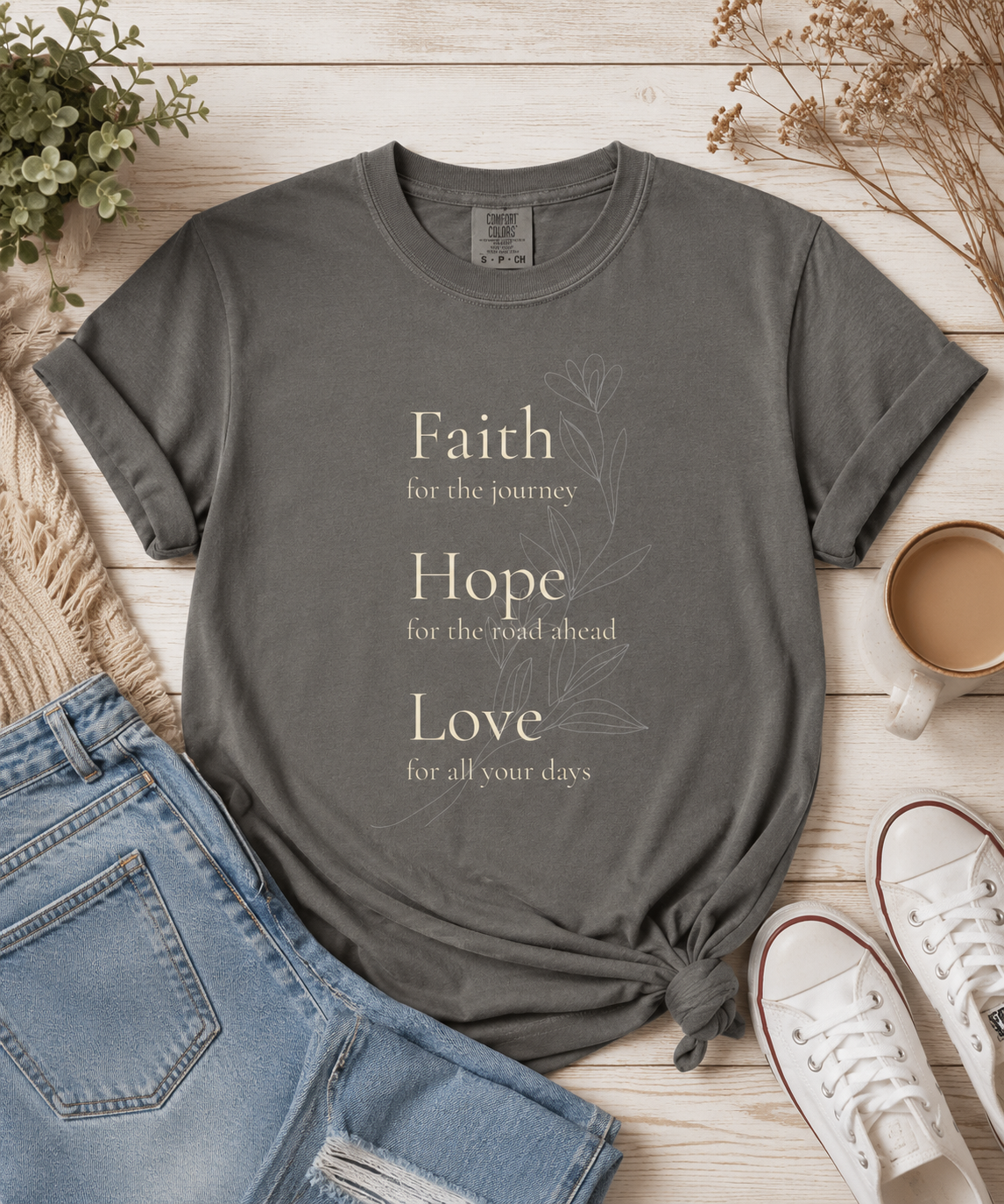 Pepper Comfort Colors t-shirt featuring a Faith Hope Love floral design styled in a warm flat lay with denim jeans, white sneakers, a coffee mug, and neutral home accents. Vintage-inspired artwork with a timeless, uplifting aesthetic.
