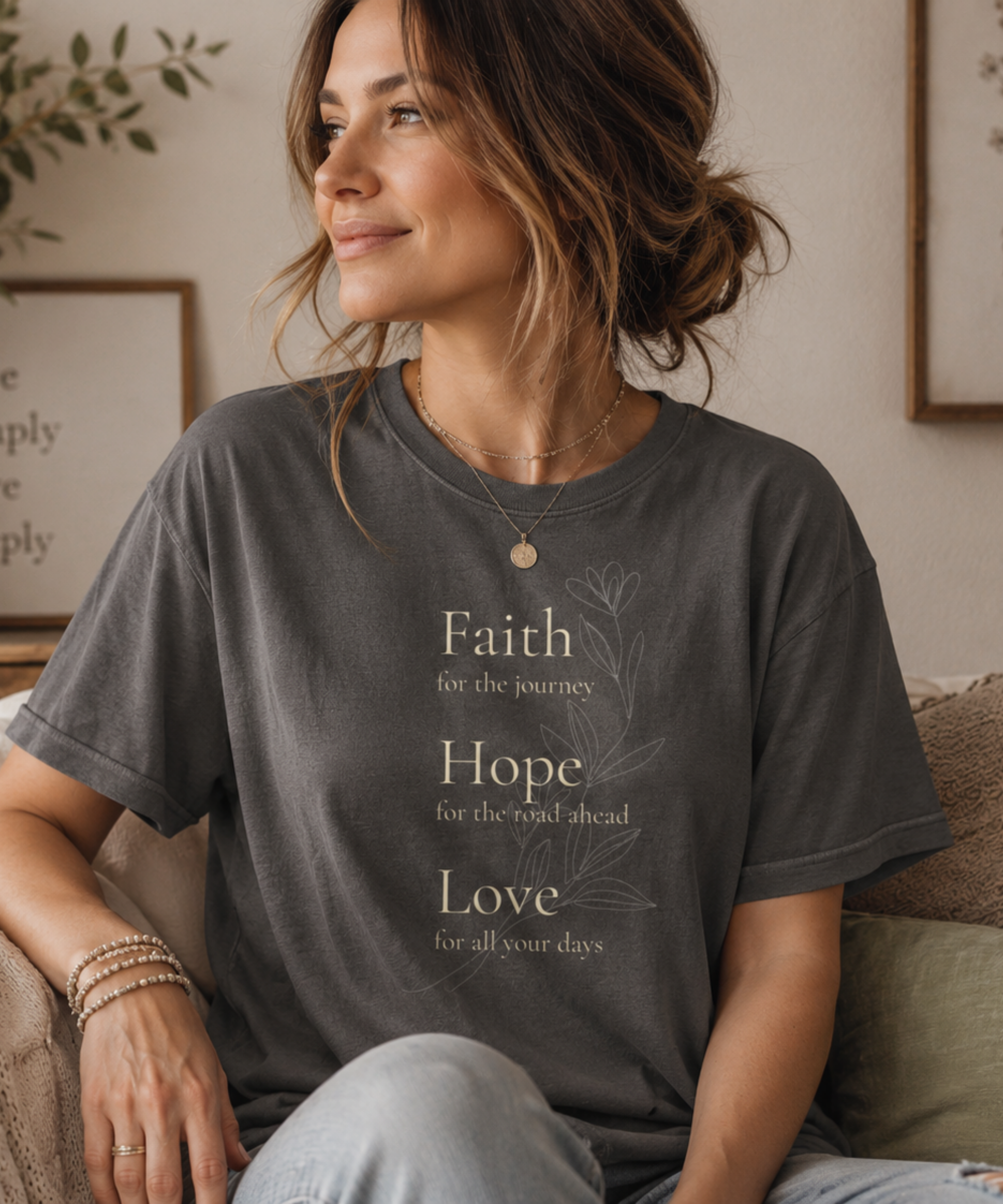 Faith Hope Love floral graphic Comfort Colors t-shirt worn by a woman relaxing in a cozy, softly lit living room. Vintage-inspired cream typography and delicate floral artwork create a peaceful, meaningful style perfect for inspired everyday living.