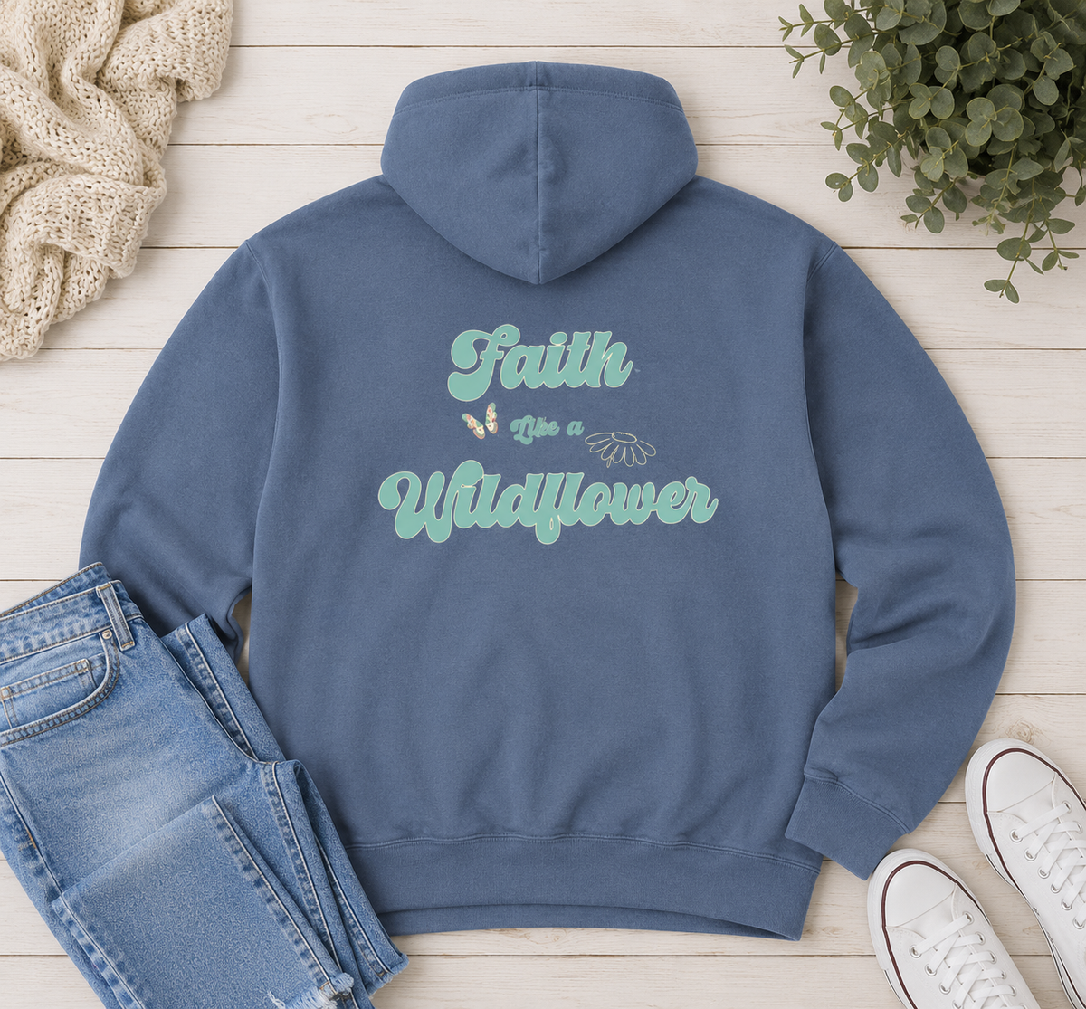 Flat lay of Comfort Colors Blue Jean hoodie featuring Faith Like a Wildflower Christian floral back design styled with jeans and neutral accessories.