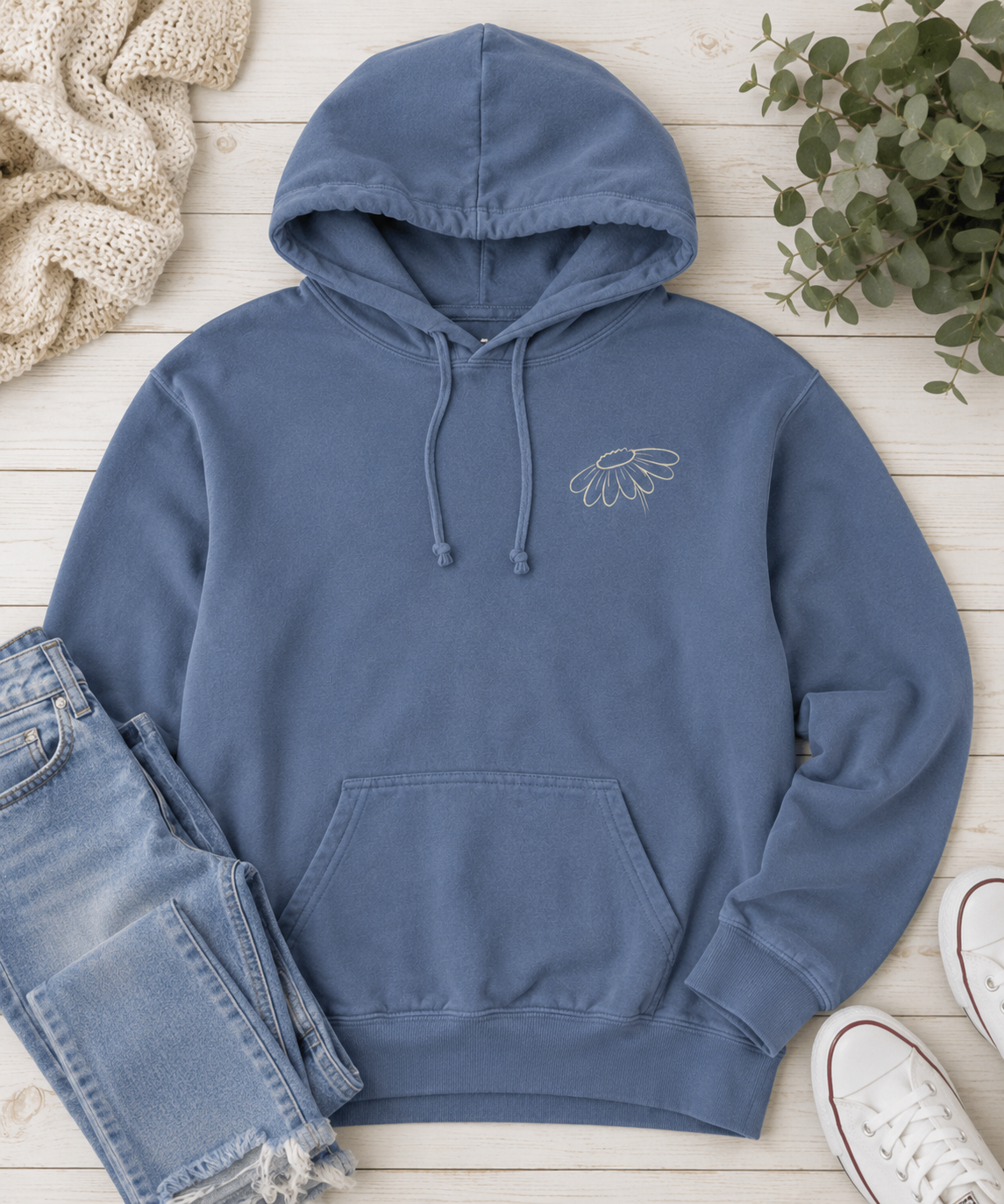 Flat lay of Comfort Colors Blue Jean hoodie with small wildflower left chest design styled with jeans and neutral accessories.