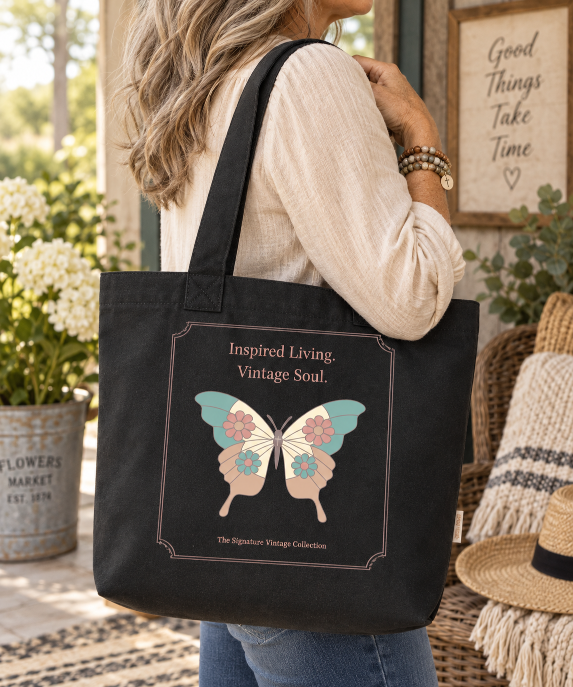 A woman wearing a cream ribbed long-sleeve top and blue jeans carries a black canvas tote bag with a vintage-style butterfly graphic and the text 'Inspired Living. Vintage Soul.