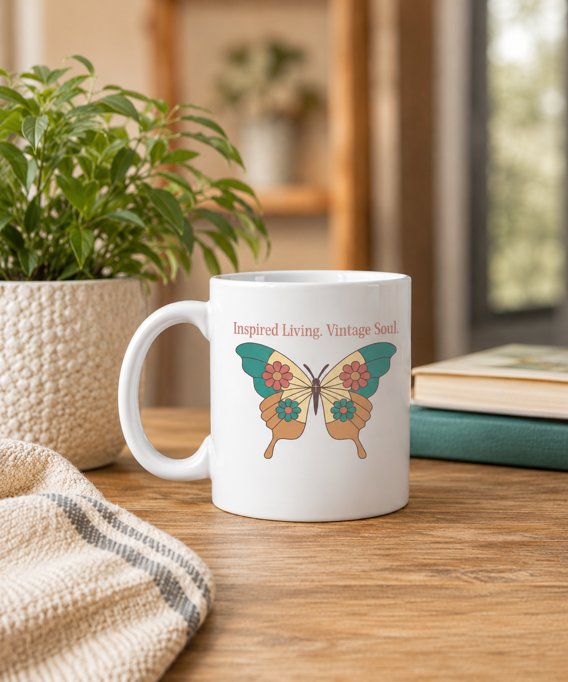 A white ceramic coffee mug with a colorful retro butterfly graphic and the text 'Inspired Living, Vintage Soul.' sits on a wooden table in a cozy, softly blurred room setting with a potted plant and books in the background.