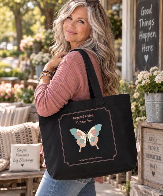 Woman with salt-and-pepper hair carrying a black Comfort Colors canvas tote bag featuring an Inspired Living Vintage Soul floral butterfly and cross design.