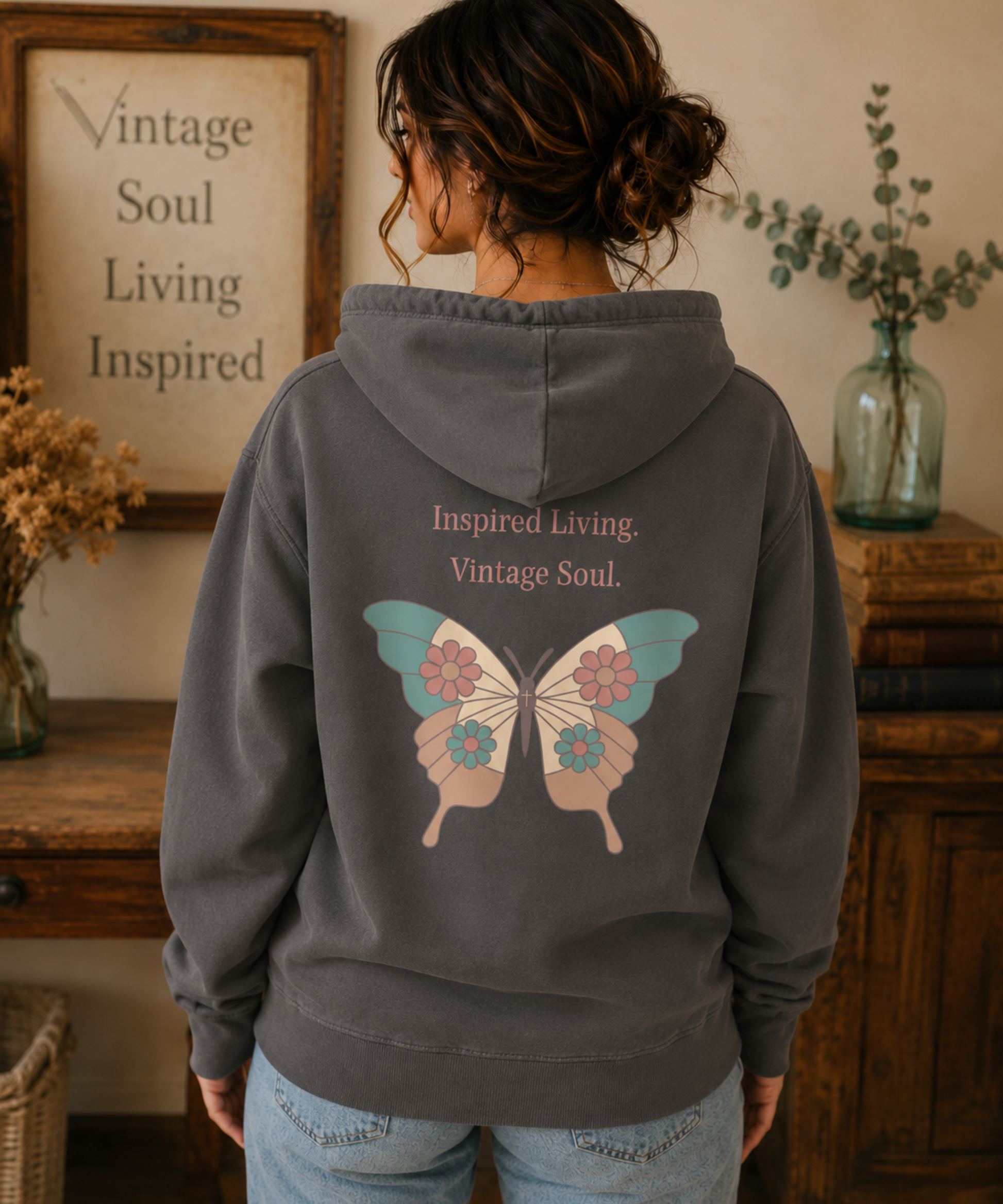 Woman wearing a Comfort Colors Pepper hoodie featuring the small "Inspired Living. Vintage Soul." left chest design in a cozy vintage-inspired home with warm wood furniture and soft neutral décor.