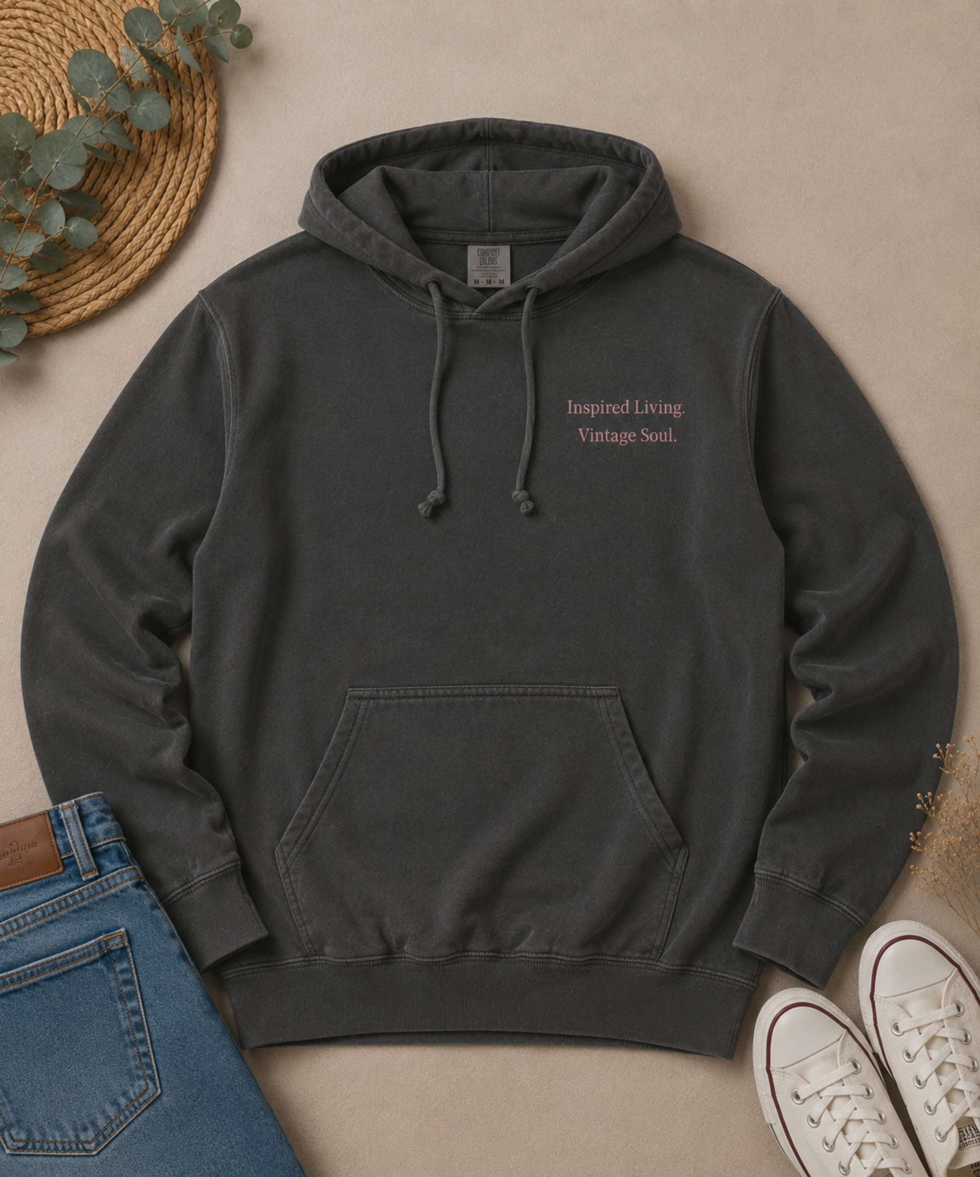 Flat lay of a Comfort Colors Pepper hoodie featuring the small "Inspired Living. Vintage Soul." left chest design, styled with blue jeans, white canvas sneakers, eucalyptus leaves, and dried florals on a neutral beige background.