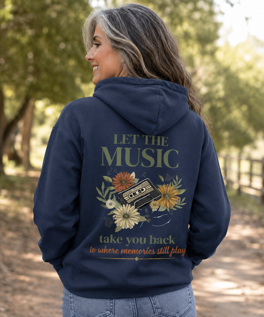 Comfort Colors True Navy hoodie featuring the Let the Music Take You Back vintage cassette and floral back design, worn by a mature woman outdoors with a nostalgic, vintage-inspired style. The front has a left chest butterfly.