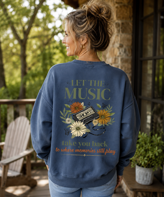 "Woman wearing a blue Comfort Colors crewneck sweatshirt featuring a vintage cassette tape, wildflowers, and butterfly graphic on the back with the phrase 'Let the Music Take You Back to Where Memories Still Play.'"