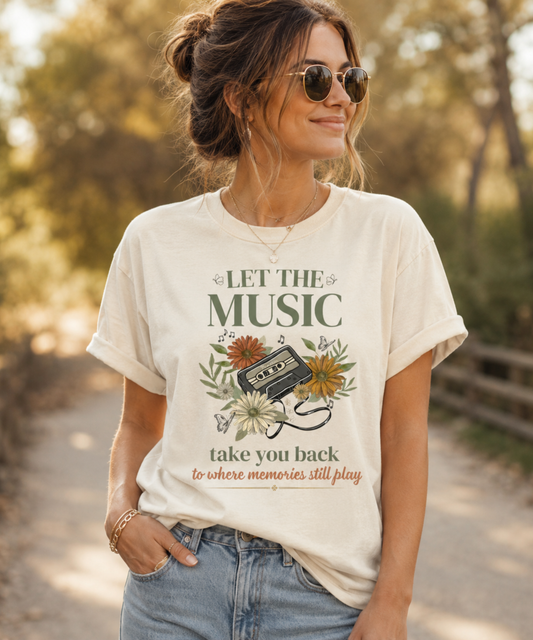 Woman wearing an ivory Comfort Colors 1717 t-shirt featuring a vintage cassette tape and floral design with the phrase "Let The Music Take You Back To Where Memories Still Play" in a warm outdoor setting.
