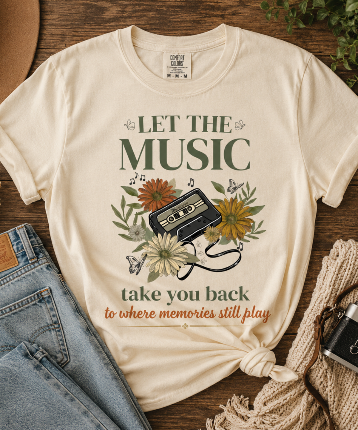 Ivory Comfort Colors 1717 t-shirt flat lay featuring a vintage cassette tape and floral graphic with the phrase "Let The Music Take You Back To Where Memories Still Play" styled with denim, camera, and a sweater.