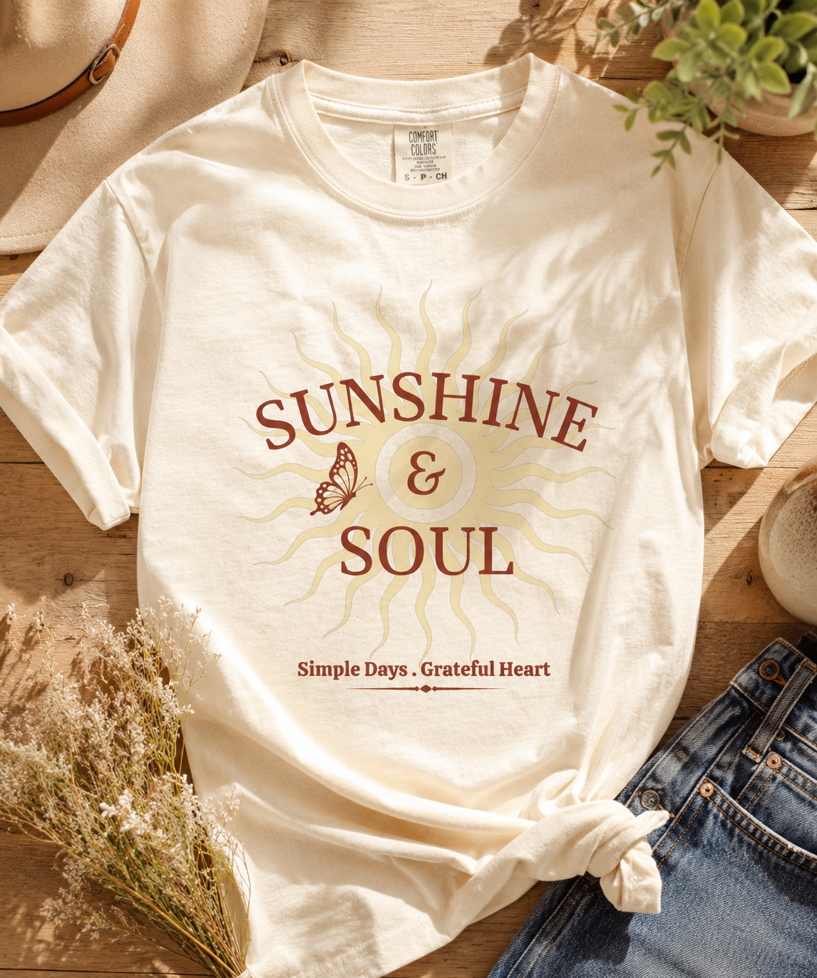 Flat lay of an ivory Comfort Colors® Sunshine & Soul t-shirt featuring a vintage sunburst graphic, butterfly accent, and the phrase "Simple Days • Grateful Heart" in warm maroon tones.