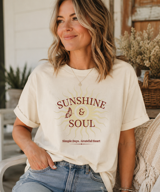 Woman wearing an ivory Comfort Colors® Sunshine & Soul t-shirt featuring a vintage sunburst graphic, butterfly accent, and the phrase "Simple Days • Grateful Heart" in warm maroon tones.