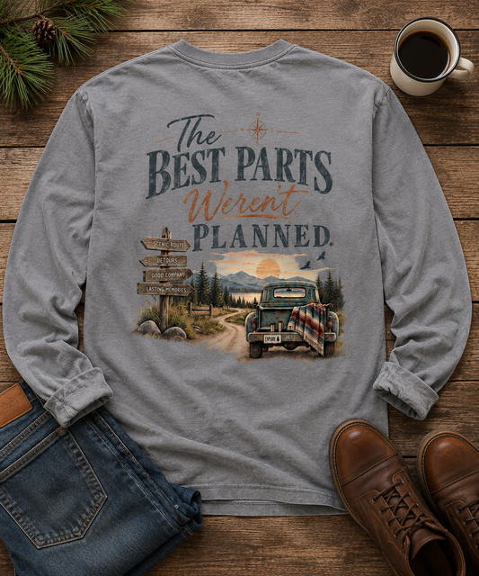 A flat lay of the back of a gray long sleeve t-shirt with a sunset mountain view and a dirt road . An old pickup truck and words that say The Best Parts Weren't Planned.